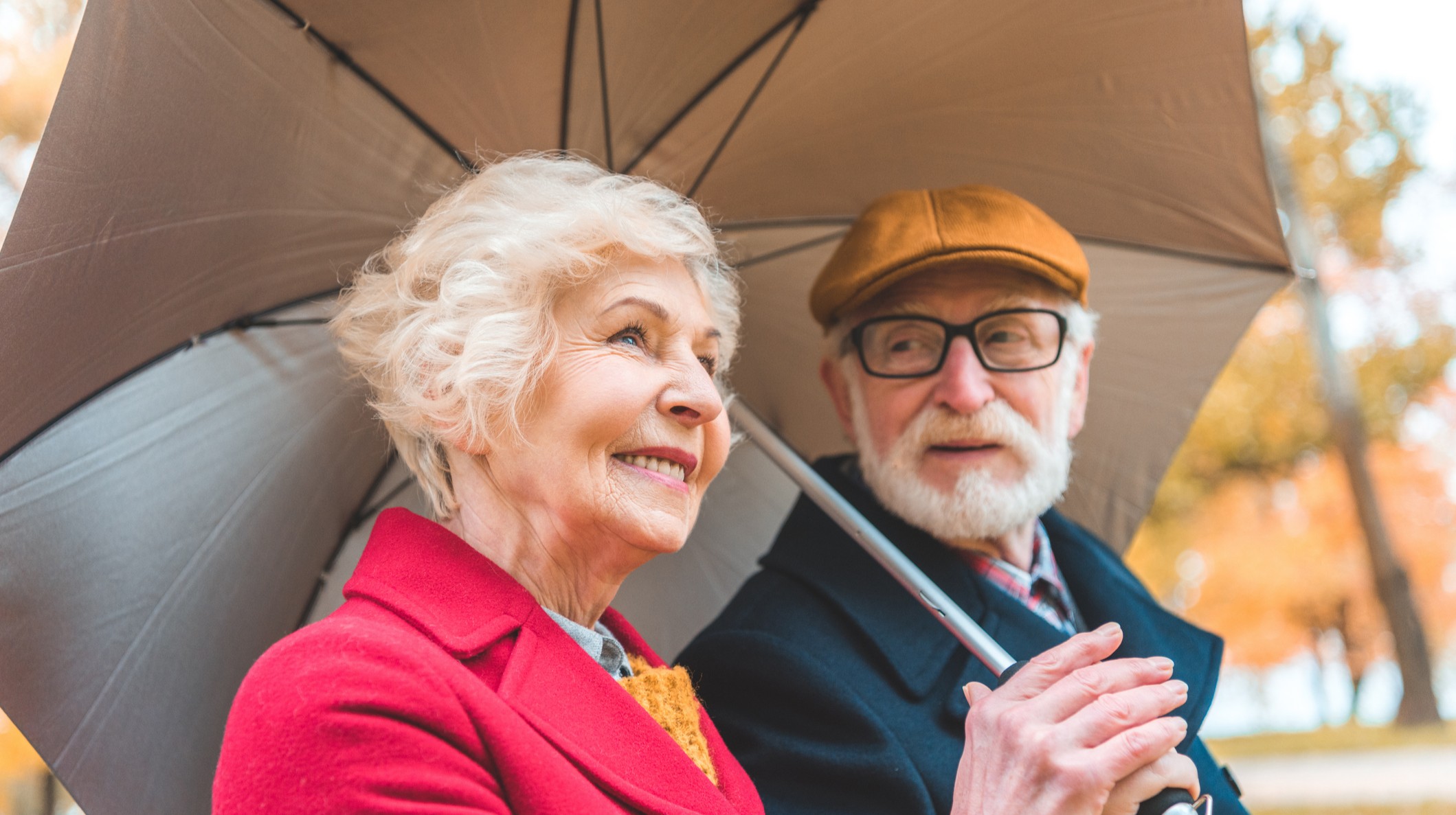 A senior couple sharing an umbrella while walking through the park.