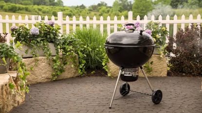 Lifestyle image of the Weber Master-Touch Charcoal BBQ 67cm sitting on a patio in a garden