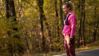 Woman wearing weighted vest along tarmac path in forest