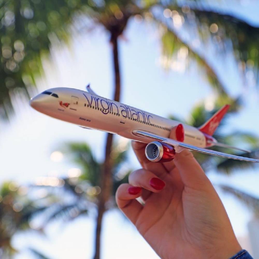 A model plane from Virgin Atlantic in front of a sunny, palm tree.