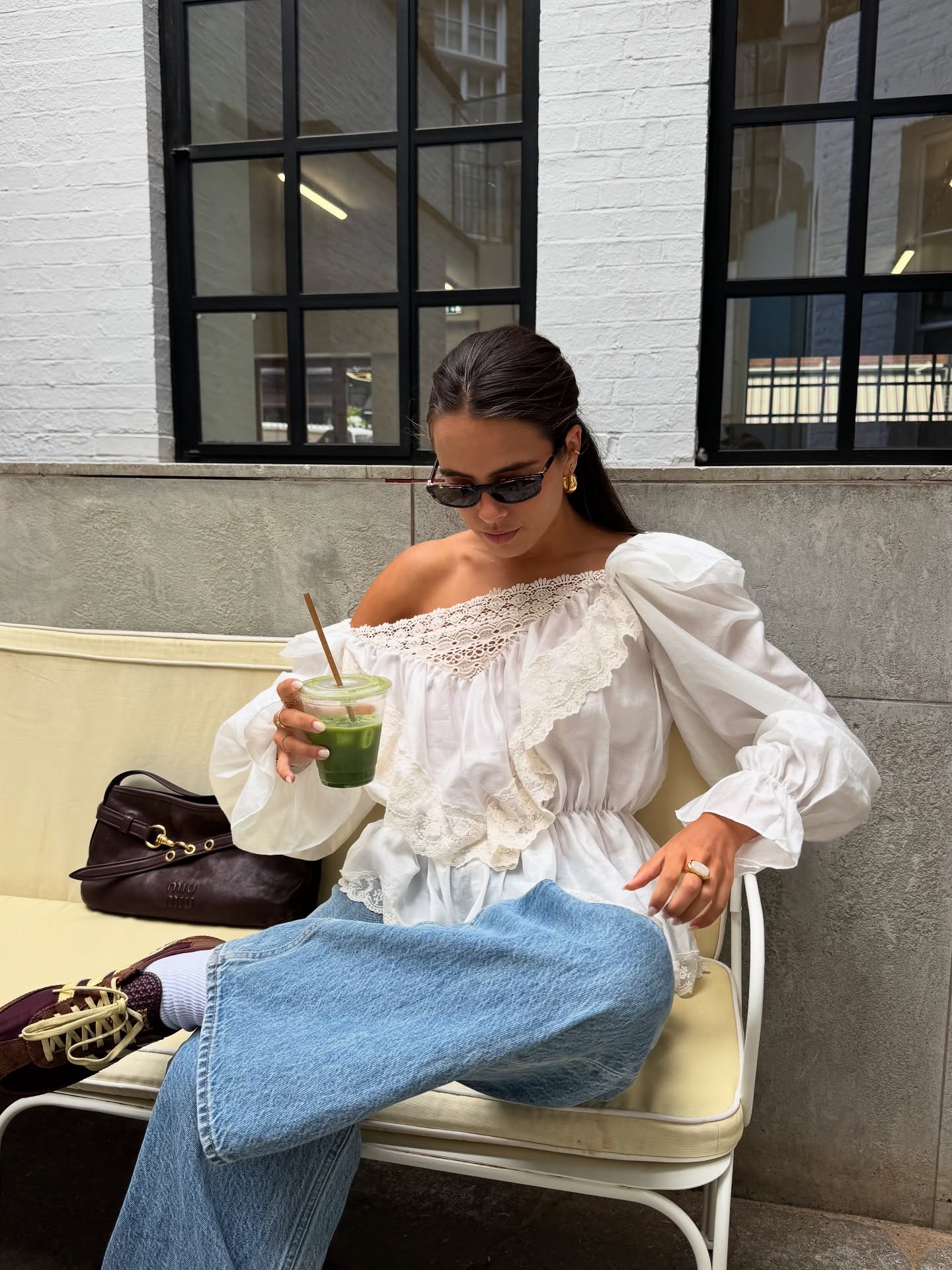 Fashion Person Tia Dewitt wears a boho outfit. She wears a lace detail top, blue denim jeans and Adidas SL 72's. She is sat looking at her jeans with a Miu Miu bag next to her in a recent image from her Instagram.