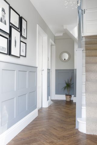 Hallway with grey panelling halfway up the walls, wooden parquet flooring and a monochrome gallery wall