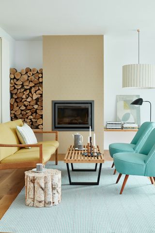 A mid-century modern living room with mustard and teal chair decor, teal and white striped rug, and wooden log fuel for central fireplace