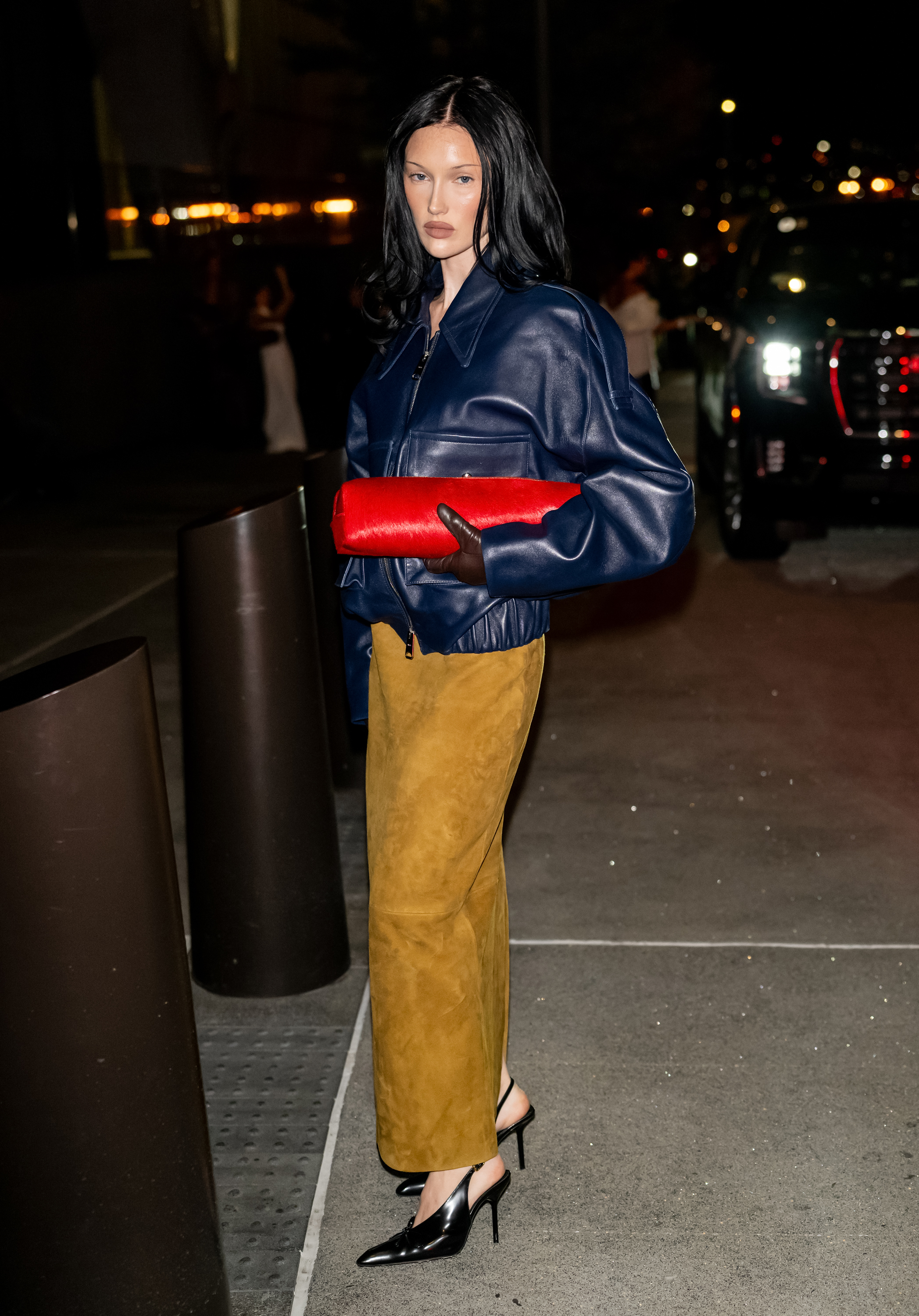 Meredith wears a navy leather jacket, red bag, and suede pencil skirt.