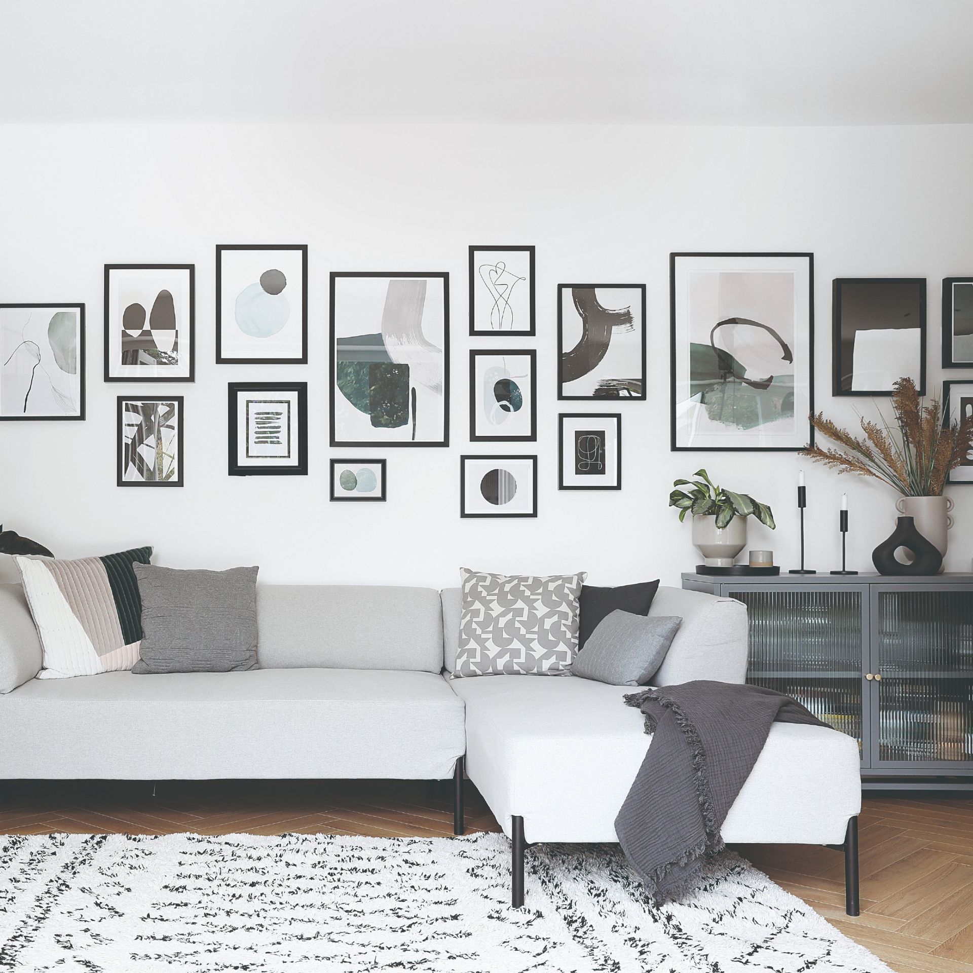 A white-painted living room with a grey chaise sofa, cabinet and accessories with black accents through gallery wall frames and sofa legs