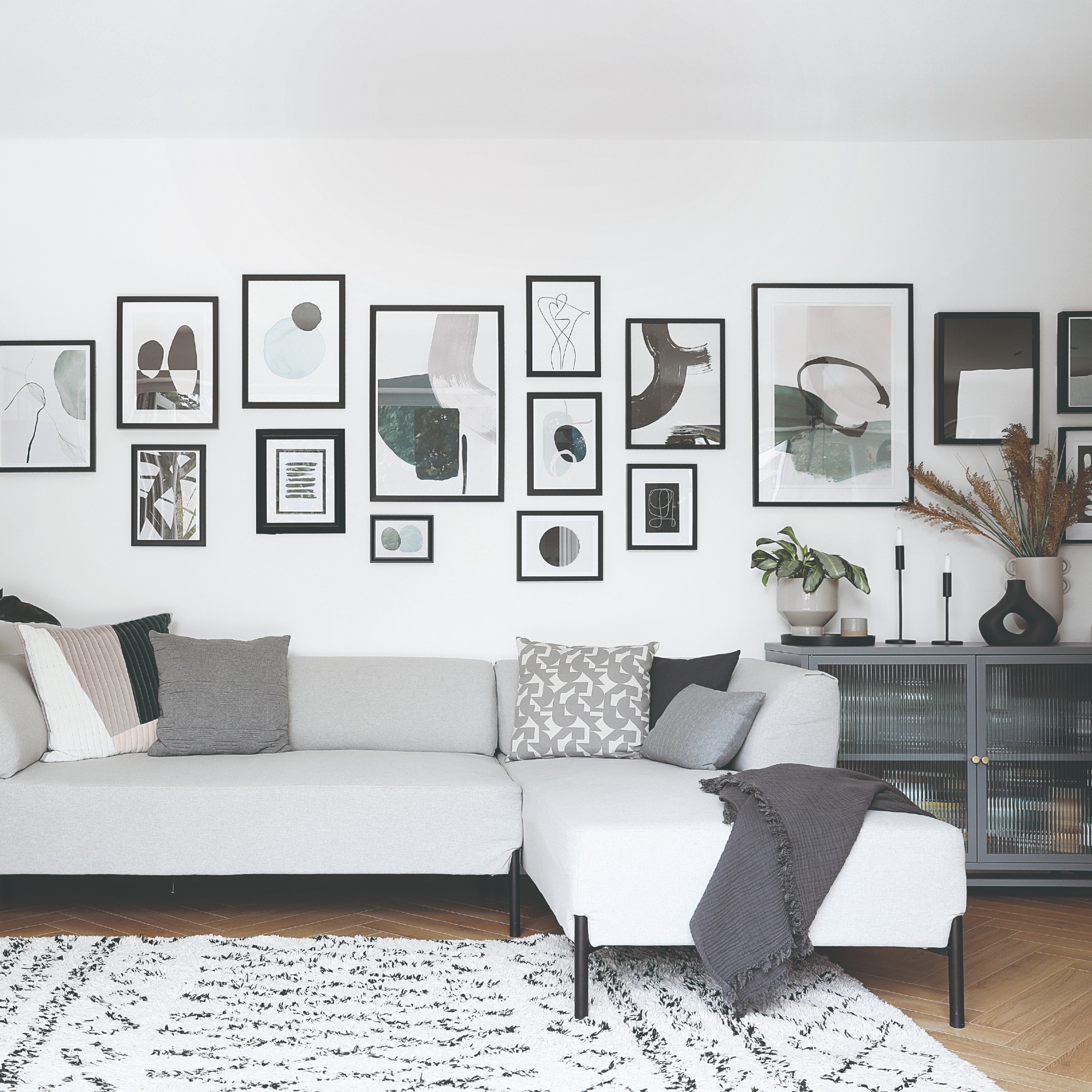 A white-painted living room with a grey chaise sofa, cabinet and accessories with black accents through gallery wall frames and sofa legs