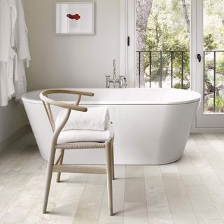 Bathroom with white bath, light wooden tiles and wood chair, with glass doors opening on to a balcony