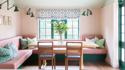 mint green and pink banquette in pink paneled kitchen with green window frame and wooden dining table