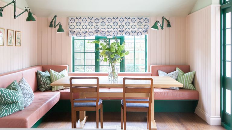 mint green and pink banquette in pink paneled kitchen with green window frame and wooden dining table