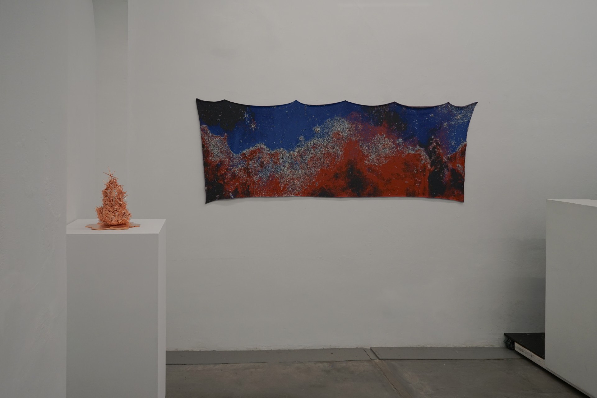 A horizontal cloth tapestry of a space photograph hangs on a white wall. 