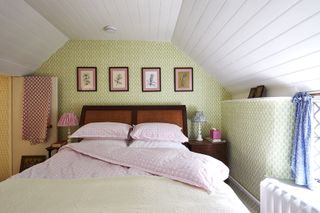farmhouse style bedroom with green print wallpaper, artwork, mahogany and rattan bed, pink bedding, pink lampshade, blue lampshade, white shiplap ceiling, blue drapes