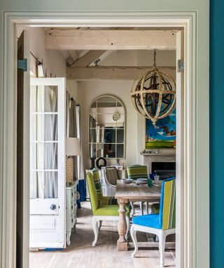 A garden room with a large wooden dining table and green and blue chairs