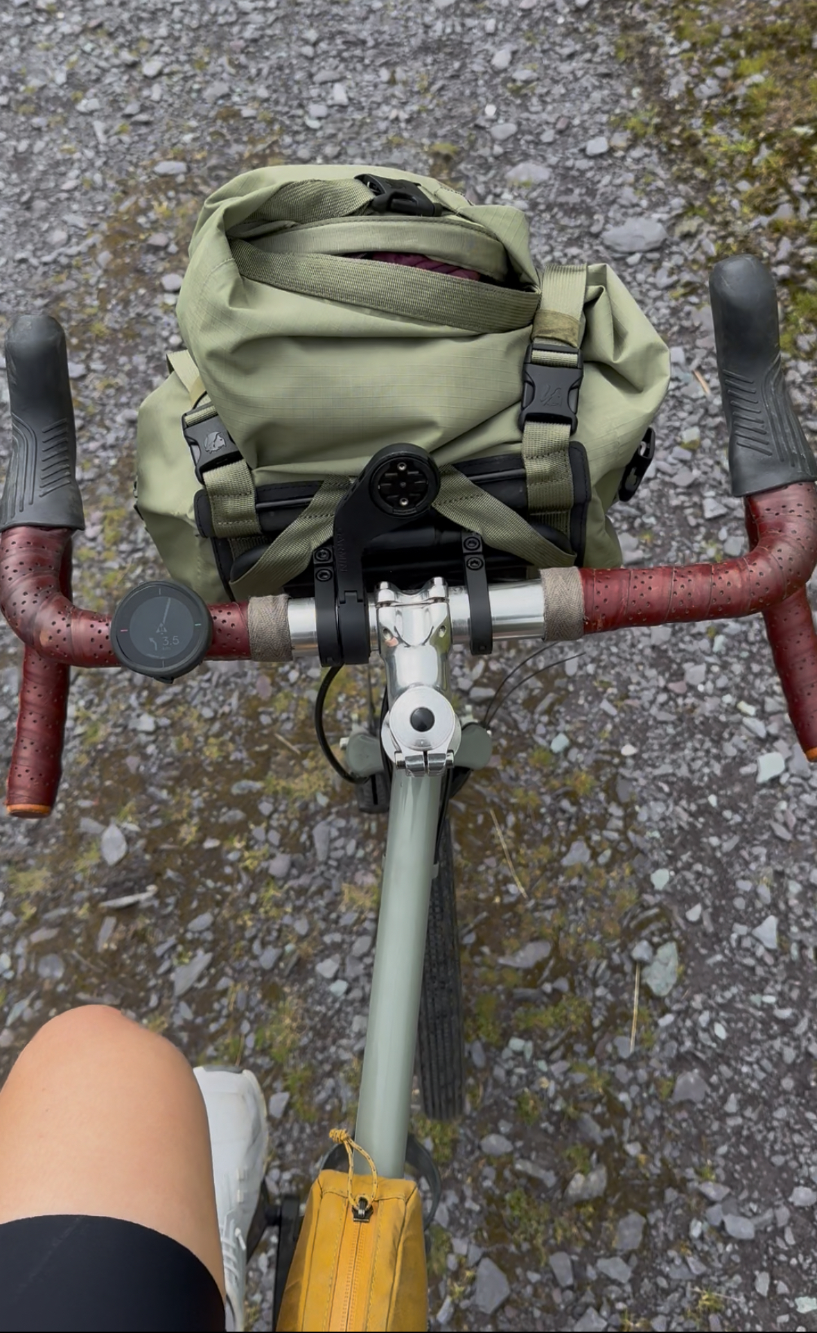 A cockpit on a bike with a green front pack and the little beeline velo on the left hand side of the handlebars.