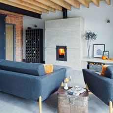 An inbuilt wood burner with a concrete surround in a large open plan living room with blue sofa and wood beams