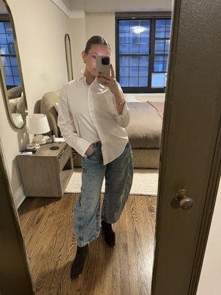 Nikki wears a white button-down shirt, barrel-leg jeans, and ankle boots.