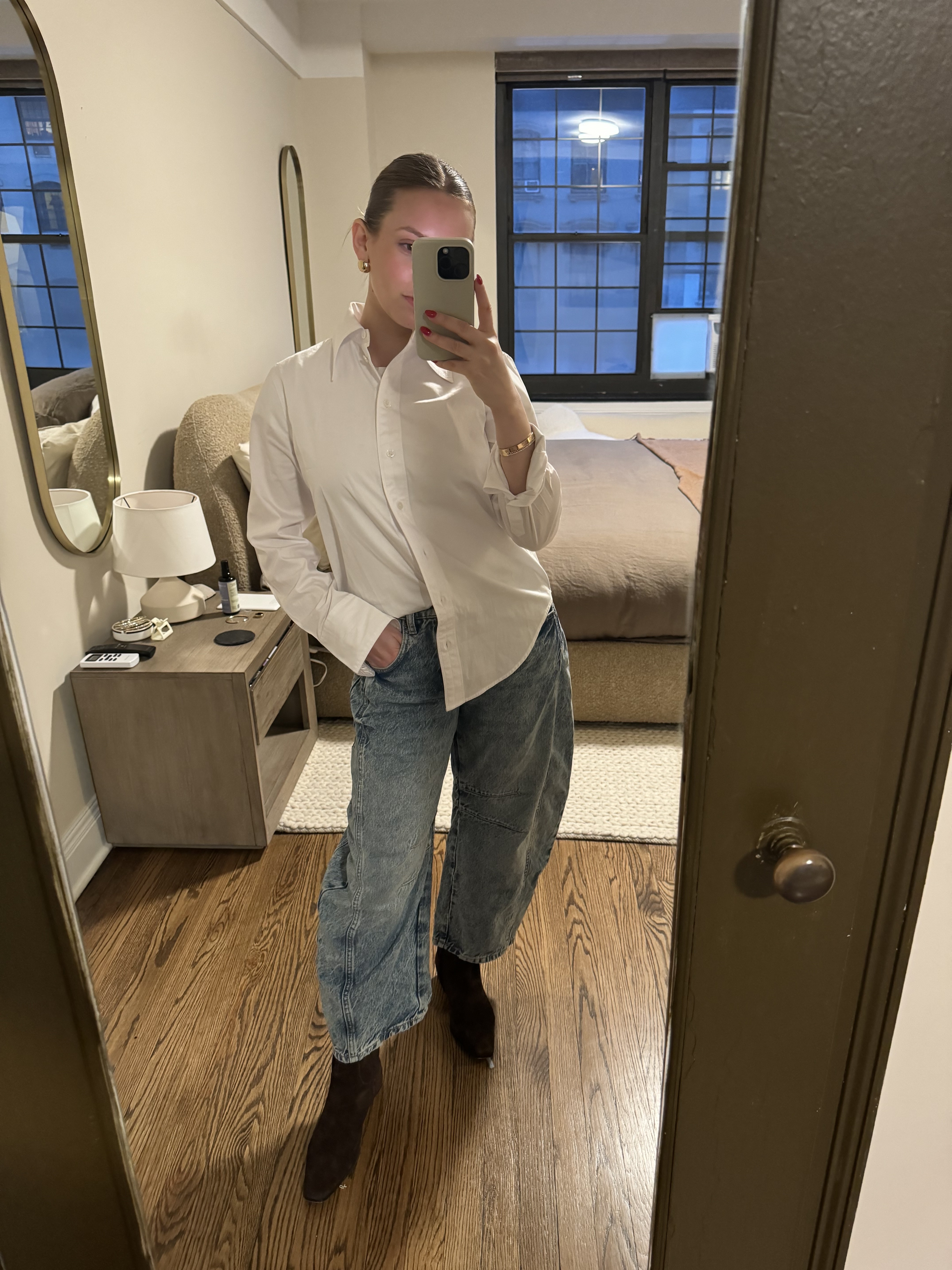 Nikki wears a white button-down shirt, barrel-leg jeans, and ankle boots.