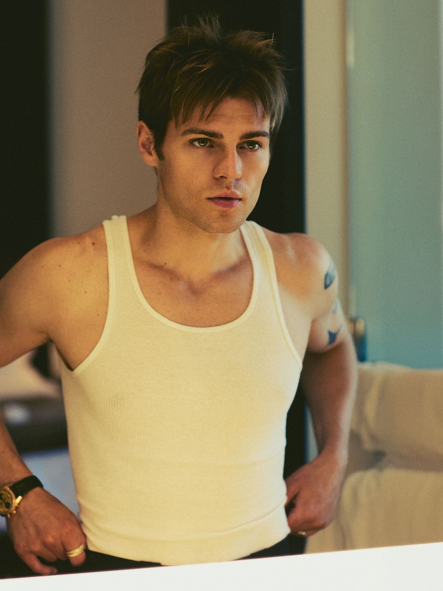 My Life With the Walter Boys actor Noah LaLonde looks at himself in a mirror. He is wearing a white tank top with black trousers and an IWC watch.