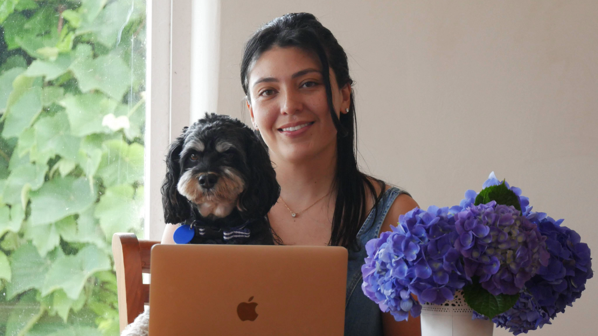 Eunice Arauz smiling with her dog in front of a laptop and flowers