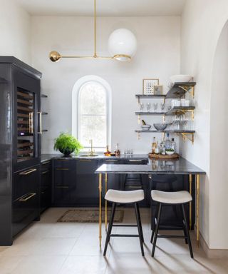 Home bar with black cabinets and worktop with gold hardware and shelving