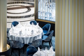 Overview of Cunard’s Queen Anne Britannia Restaurant. A round table stands against a blue carpet and a golden column