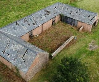 A building plot with a brick one-storey farmhouse