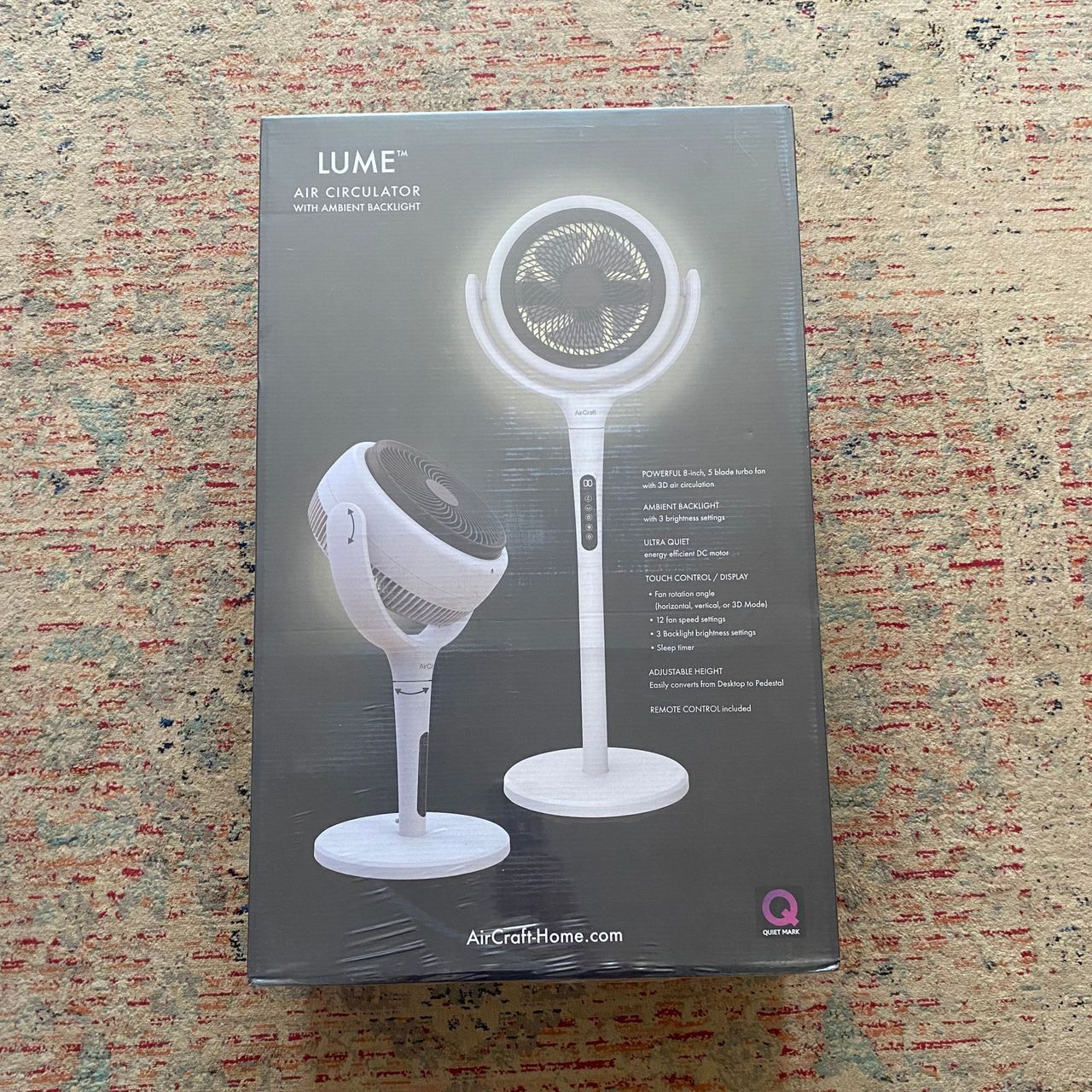 Outer packaging of the AirCraft LUME Quiet Air Circulator Fan on a beige, grey and red patterned rug