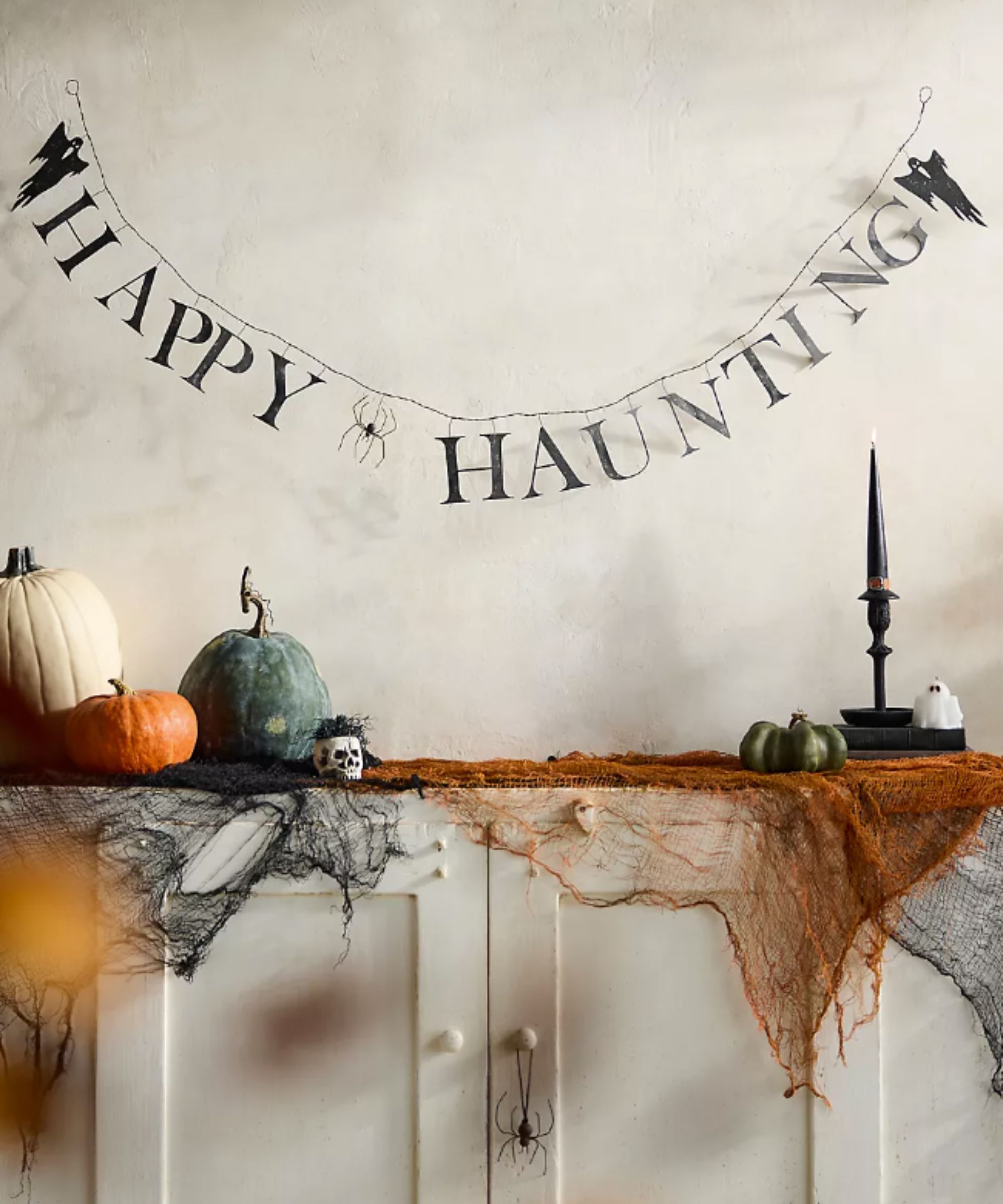 Happy Haunting iron garland hung on a wall above Halloween decorations