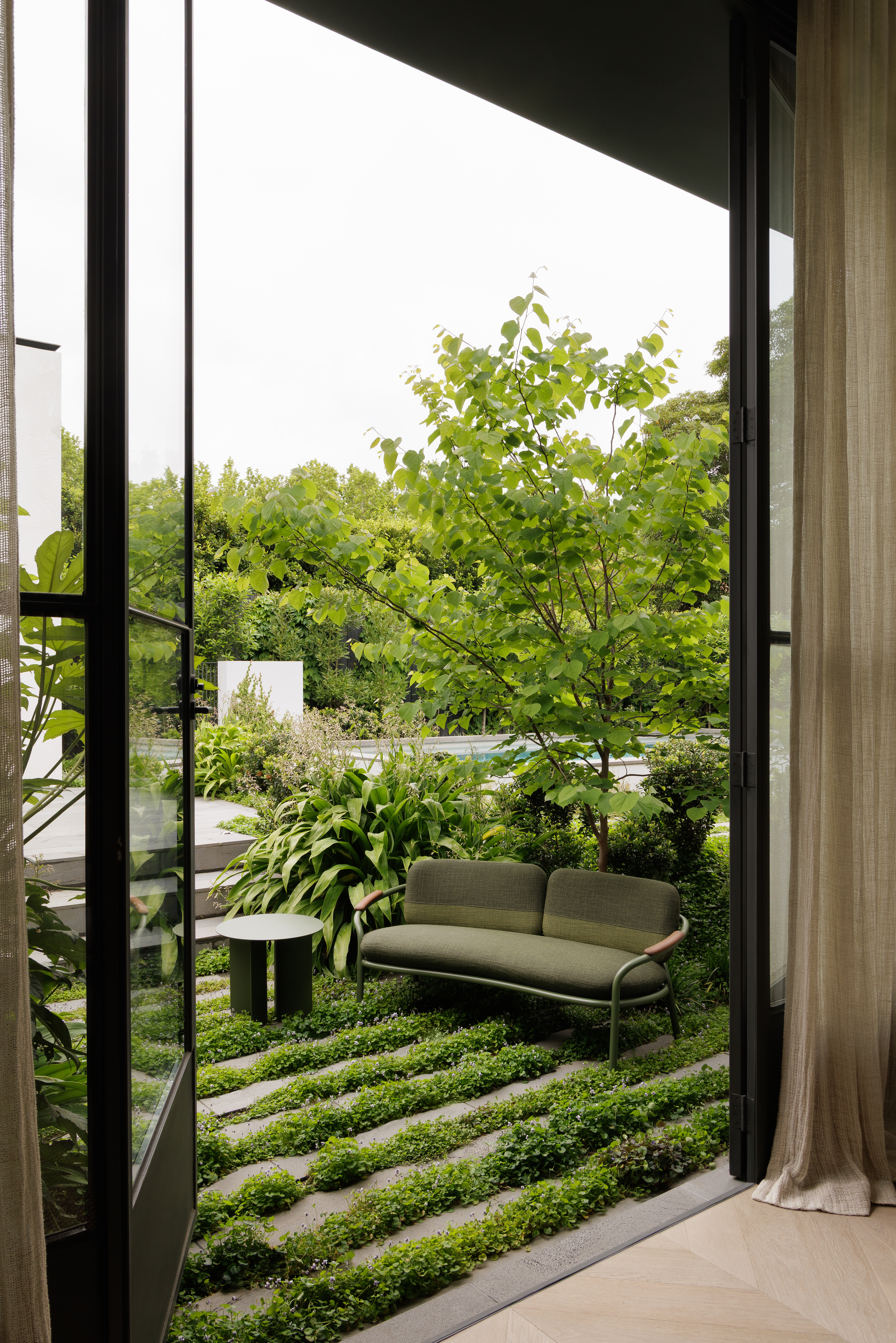 Green upholstered two-seater outdoor sofa on small terrace with verdant planting