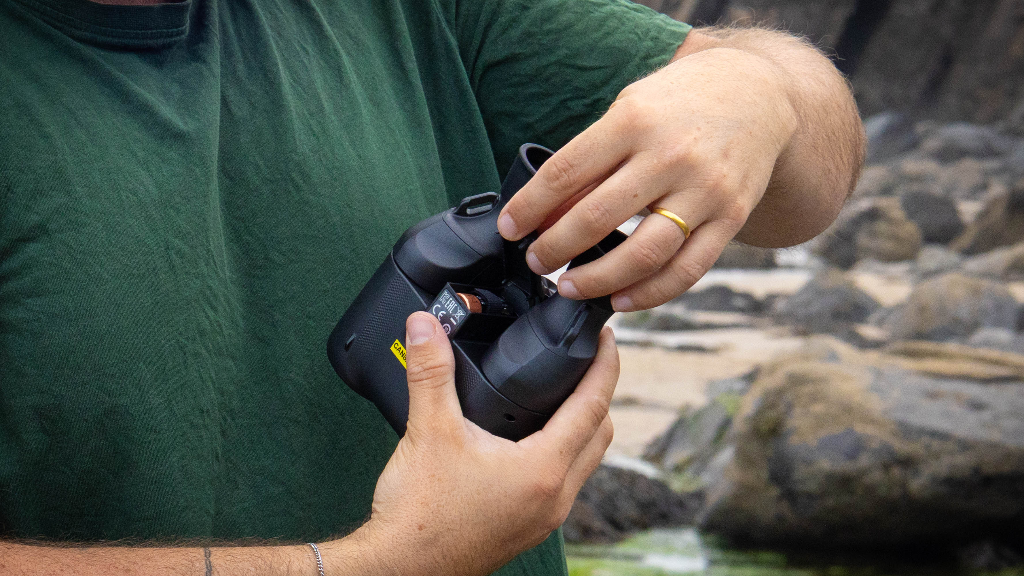 A person holding the Canon 8x20 IS binoculars and showing the battery compartment for the IS.