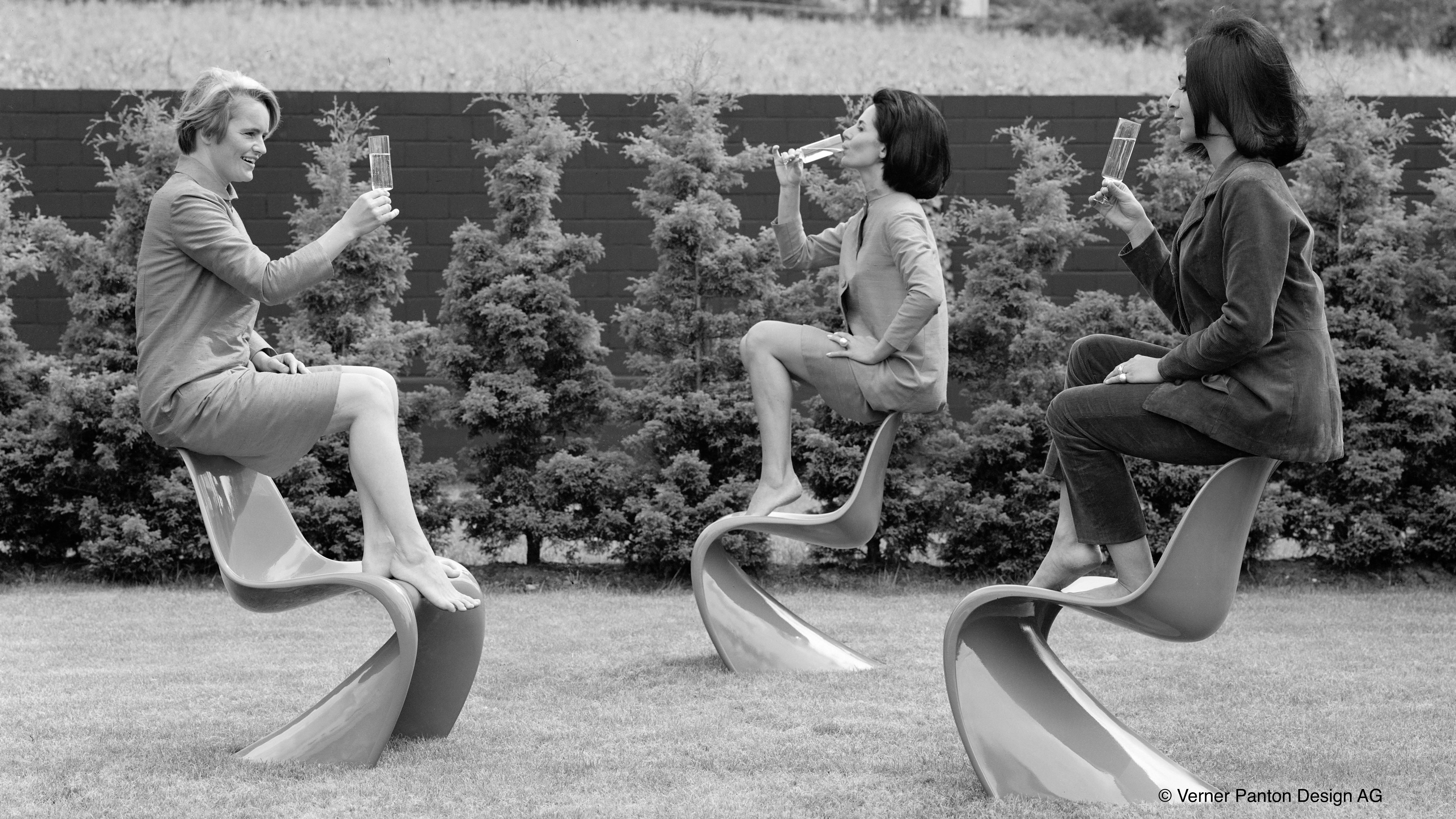 Three women drinking champagne while balancing on Panton chairs