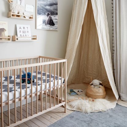 Wooden cot with bars next to beige canopy