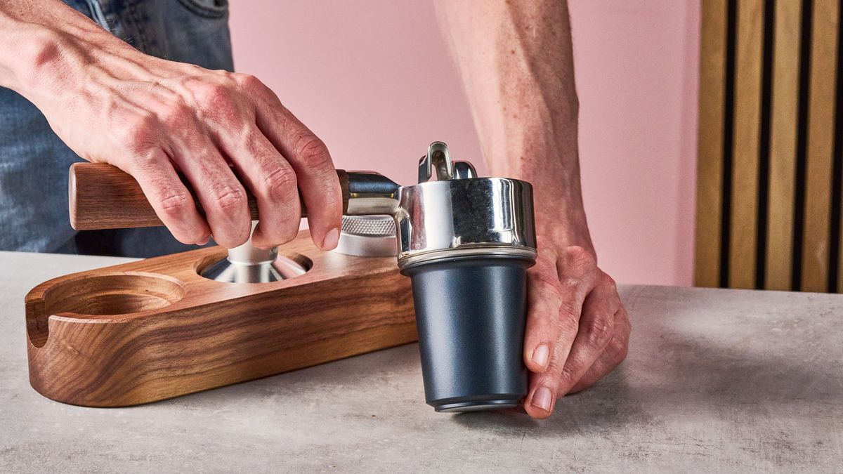 A man is placing the Meraki Espresso Machine's portafilter upside down on top of the dosing cup.