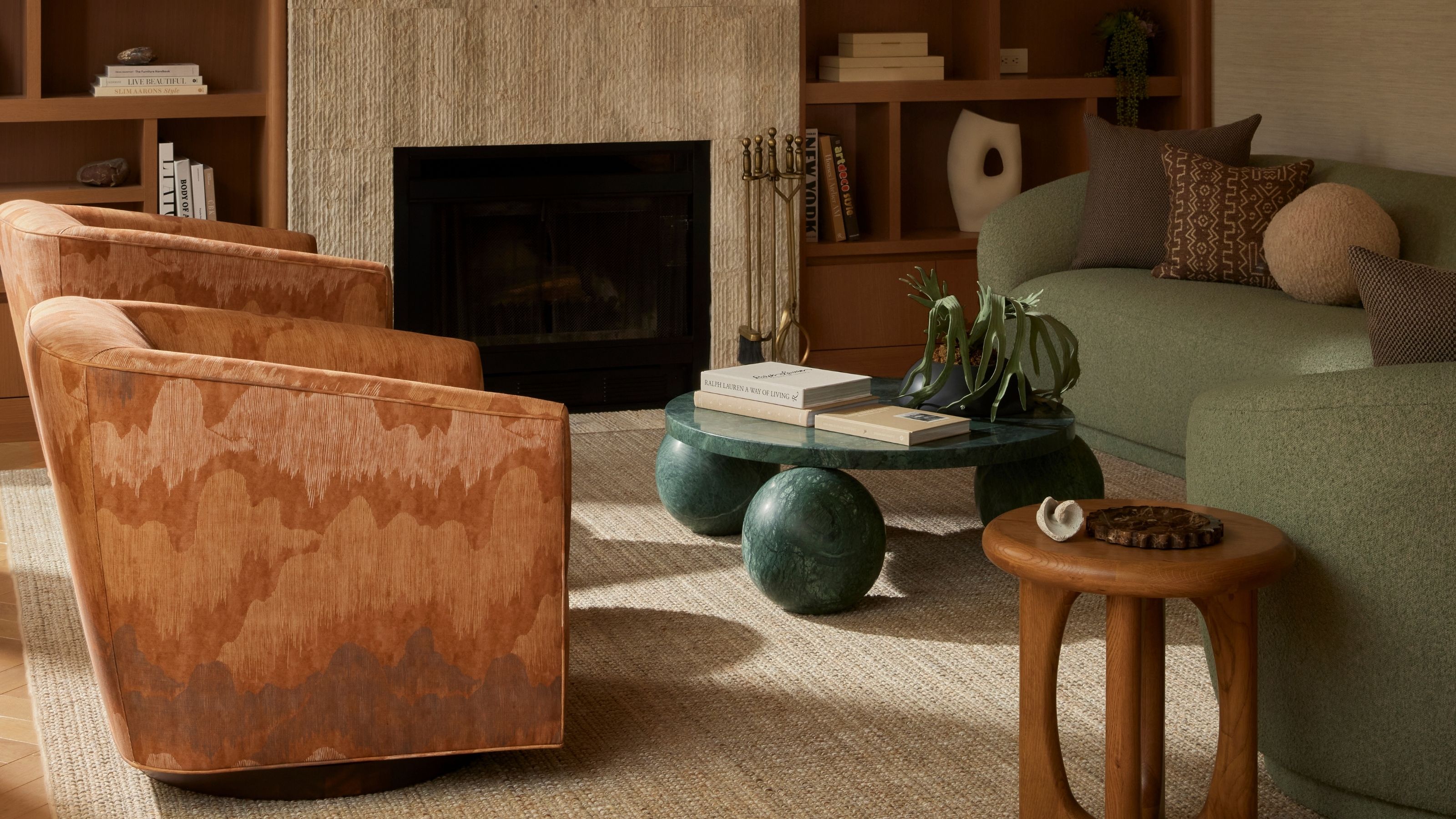 A living room with two gradient brown, velvety armchairs, a stone coffee table sitting on three petrol green spheres, a smaller one in wood, and two matching love seats in pale green.