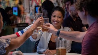 Gina Rodriguez as Mack toasting her drink with friends.