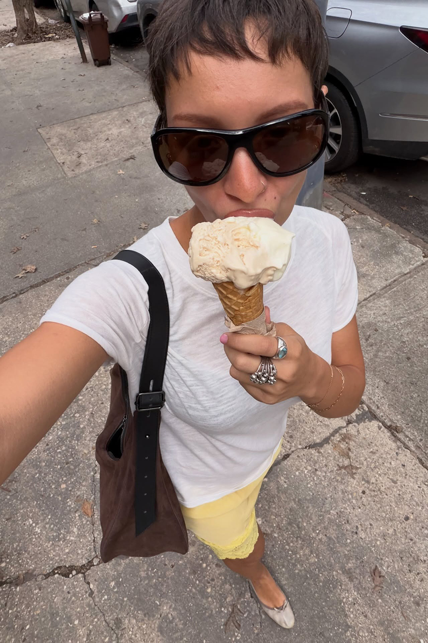 a woman wearing a white tee, yellow lace-trim skirt, brown suede bag, and brown big sunglasses