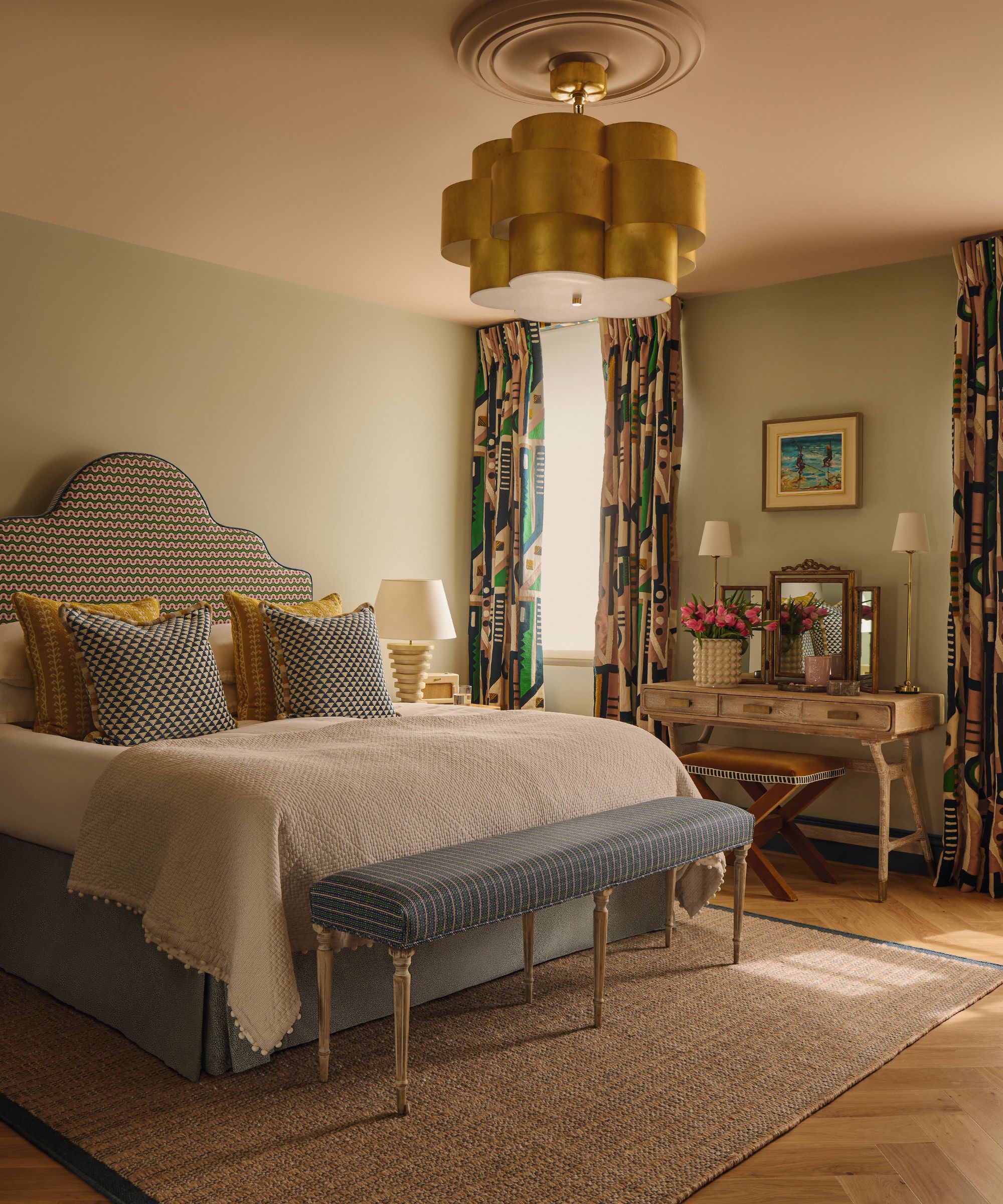 a pastel green primary bedroom with a soft pink painted ceiling, blue upholstered bed with scalloped headboard and printed drapes