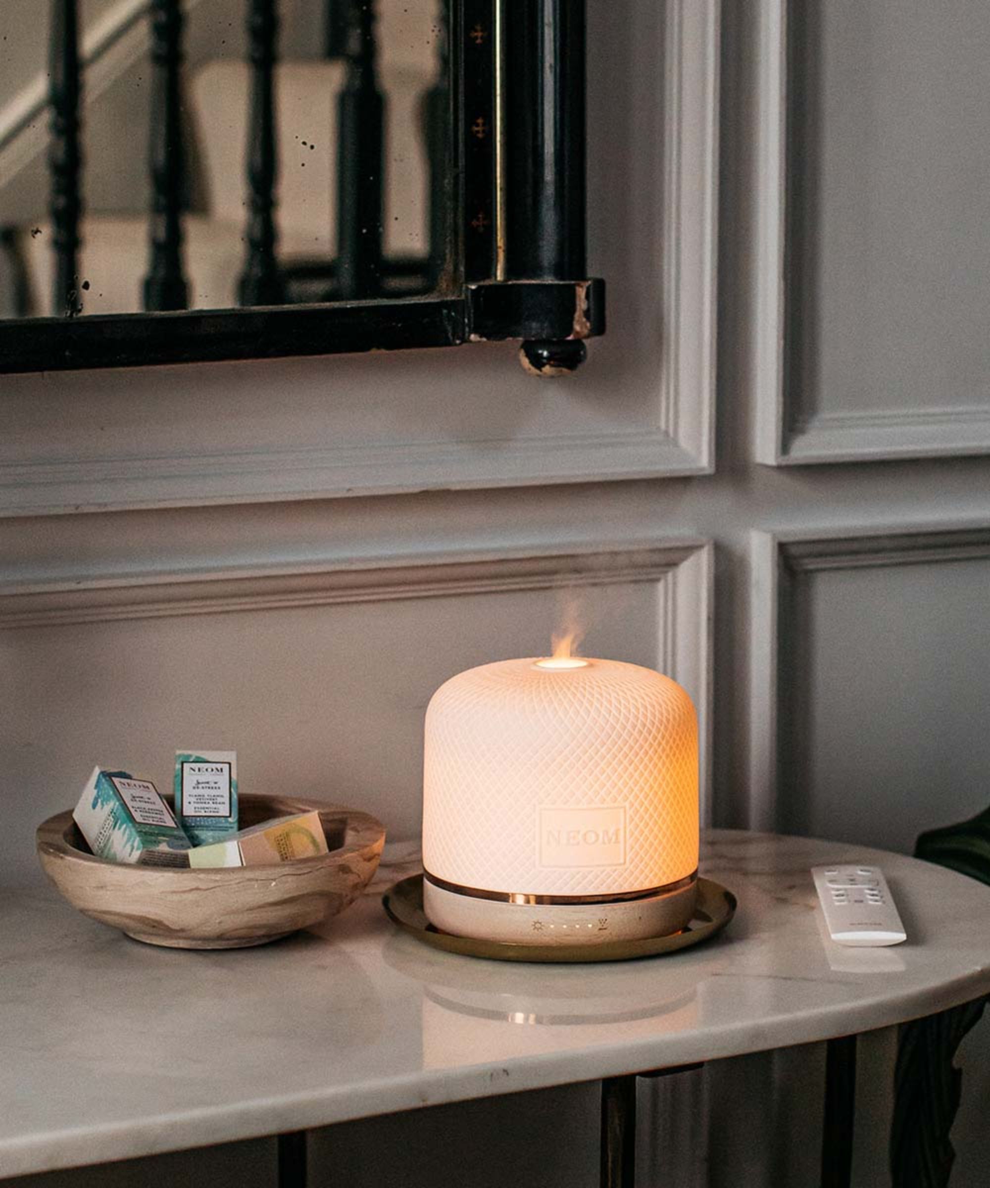 NEOM Wellbeing Pod Luxe on marble table with a white remote control and boxes of essential oils next to it
