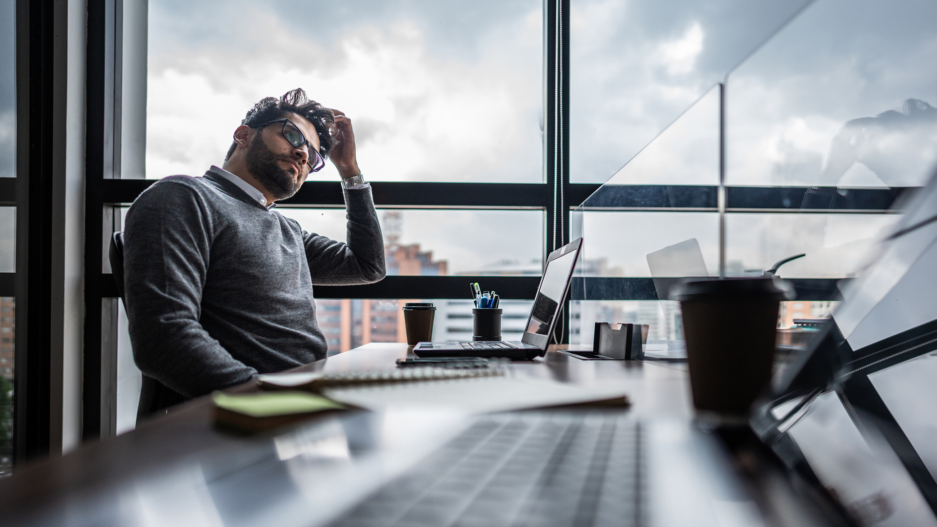 A photo of a bored-looking worker sat at a desk, not looking at their laptop screen, shot from a low desk-level angle.