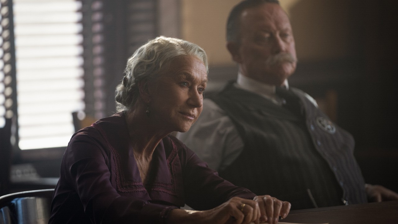 Helen Mirren sentada en una mesa con el Sheriff McDowell (Robert Patrick) sentado a su lado.