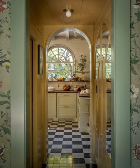 A view through an arched doorway into a white kitchen with black and white checkerboard floors