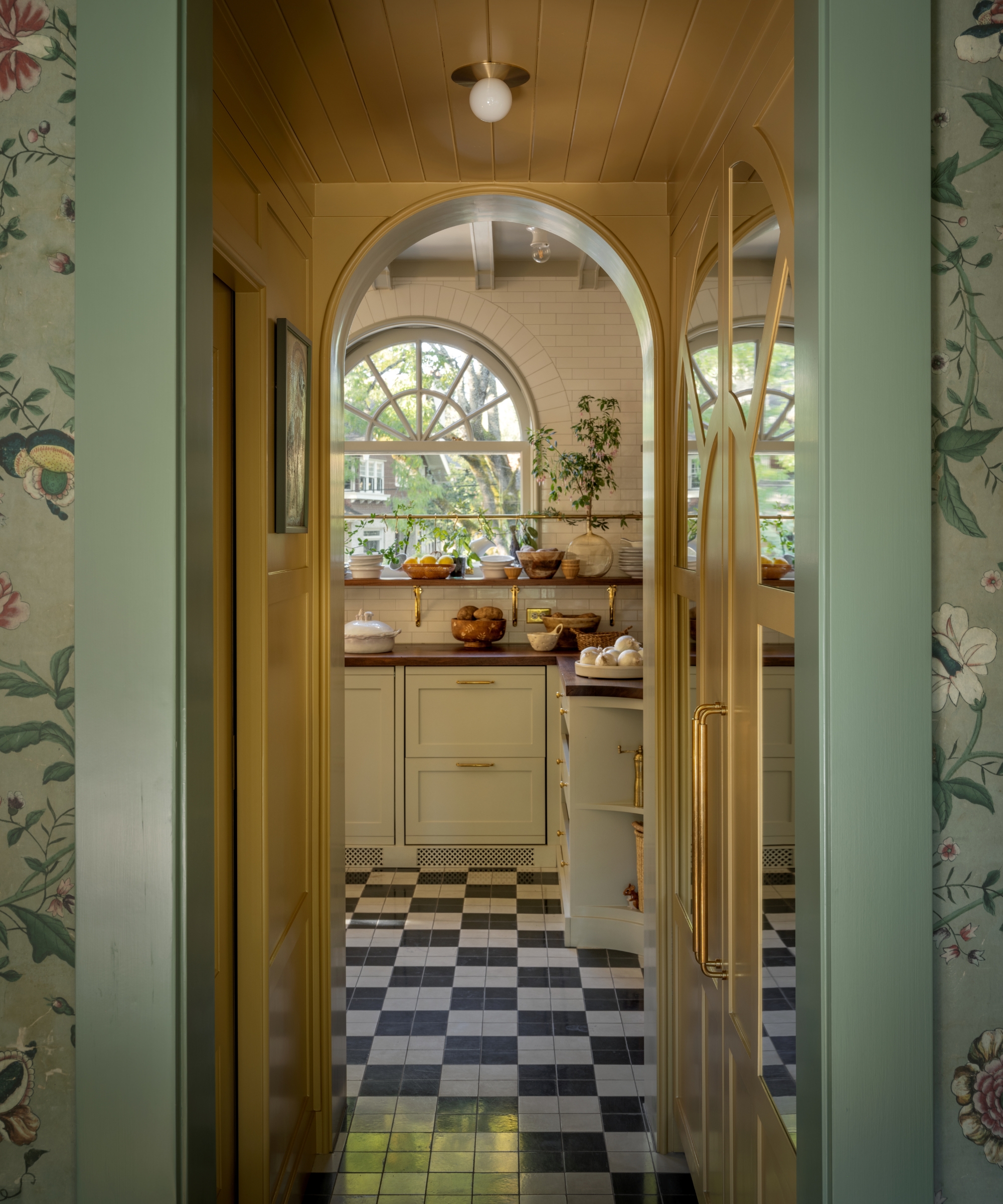 A view through an arched doorway into a white kitchen with black and white checkerboard floors