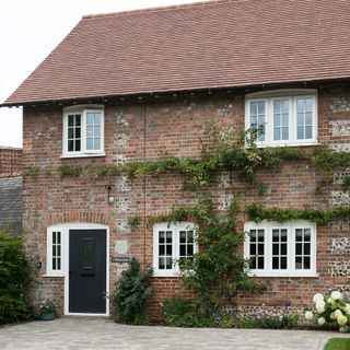 exterior of brick and flint cottage with climbing roses and new roof