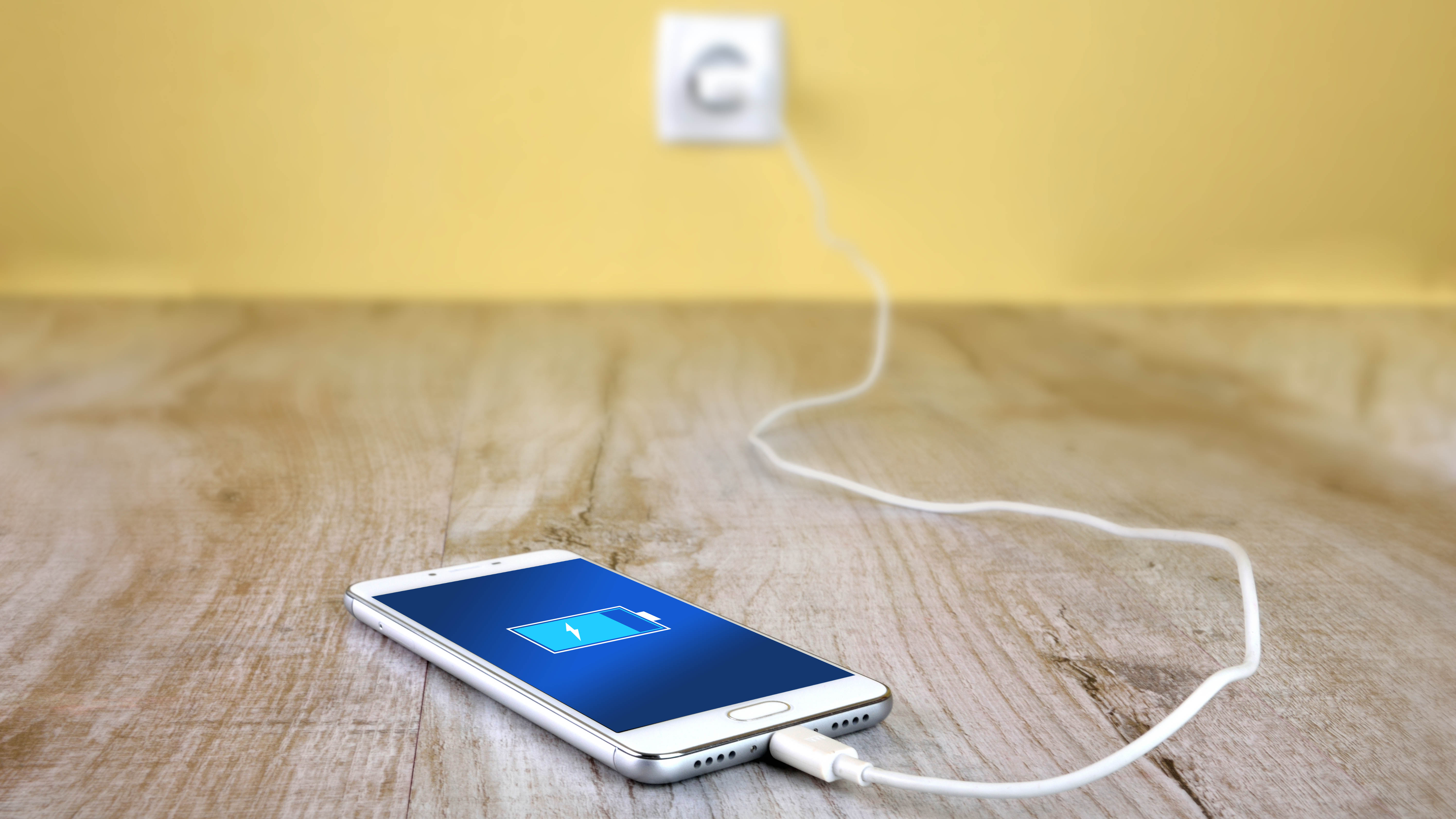 A phone laying on a wooden floor, being charged via the wall outlet