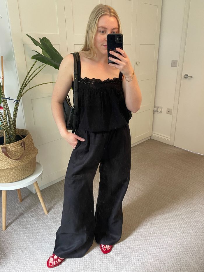 Woman wears black top, black linen trousers and red sandals