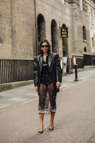 Woman wears black embellished sheer skirt, black, top, heels, and black leather jacket in the street