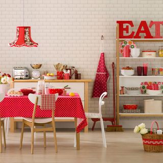 A dining room with white brick effect wallpaper and red accents in soft furnishings and accessories