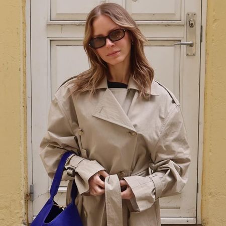 Nikki wears a trench coat with a purple bag.