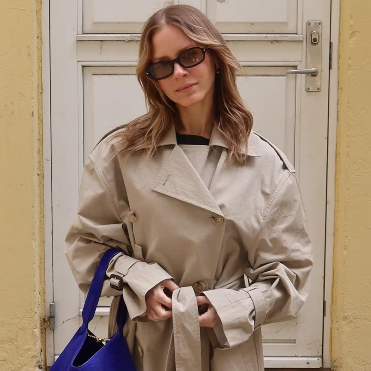 Nikki wears a trench coat with a purple bag.