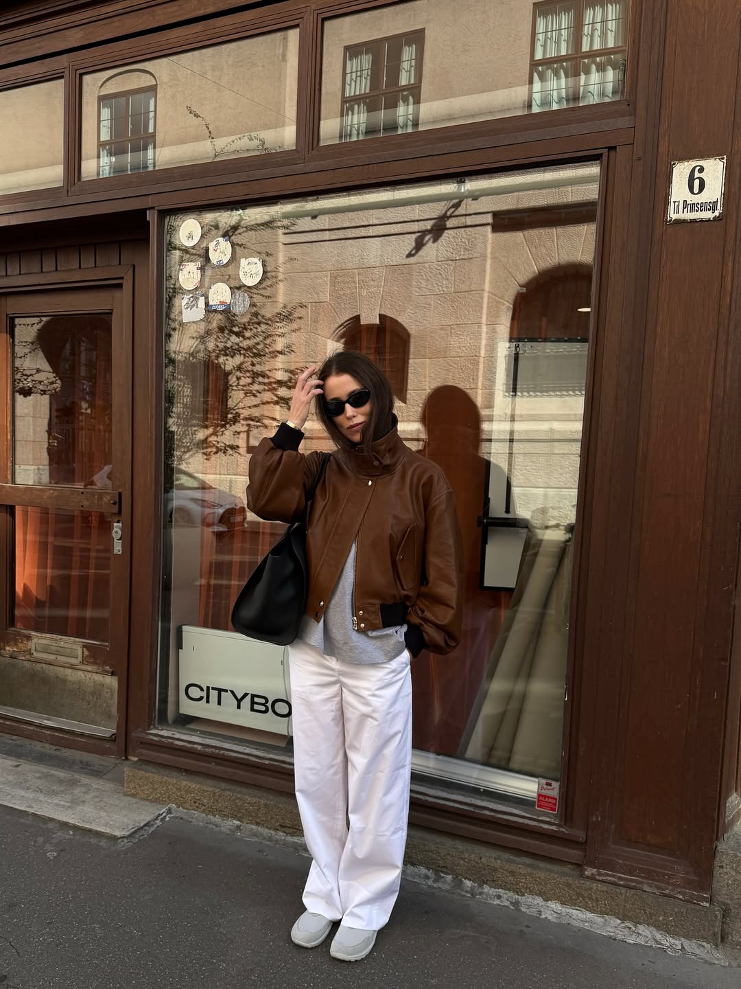 Influencer Annabel Rosendahl in a brown bomber jacket, white wide-leg pants, and sneakers.