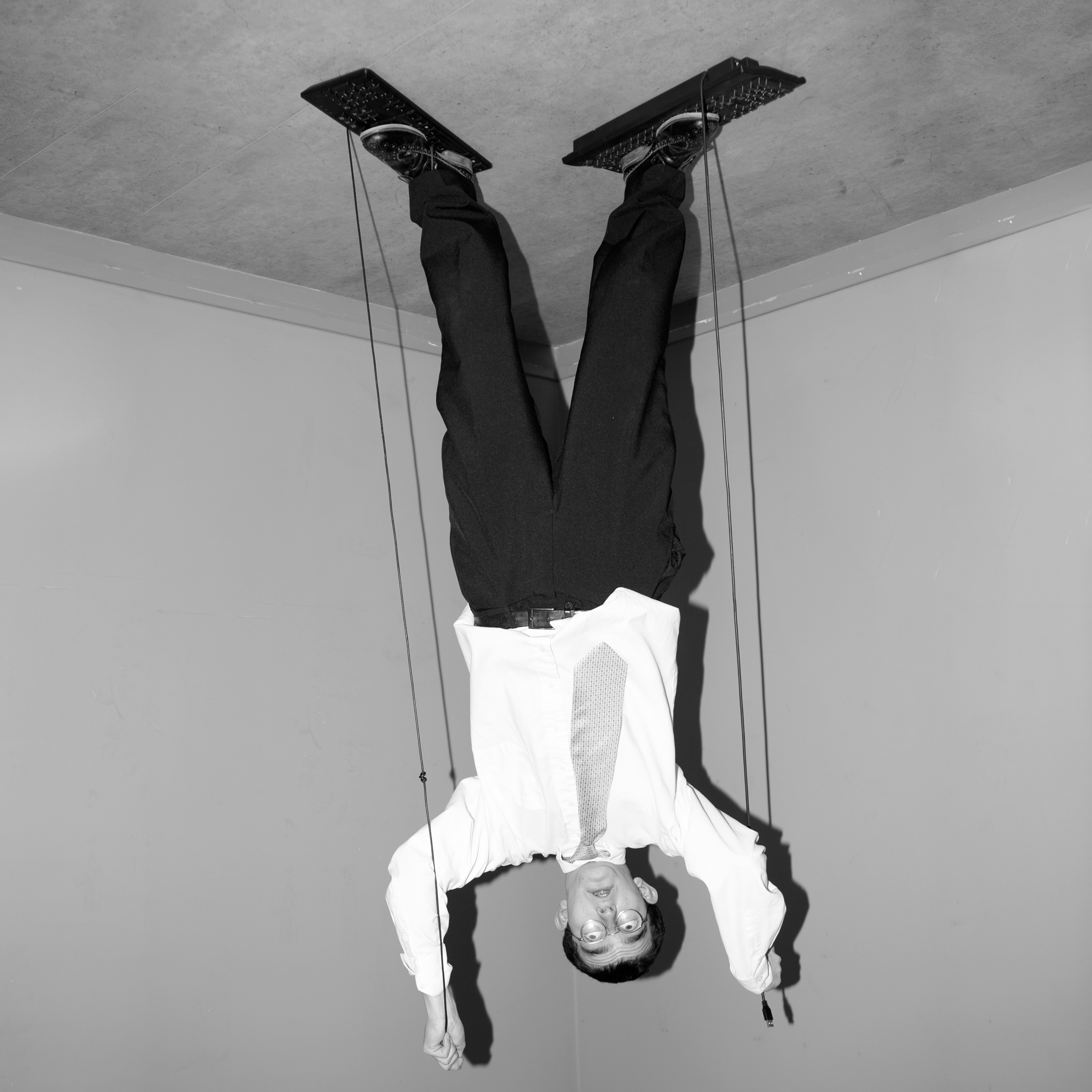 An upside down, black and white photo of a man standing on the ground wearing a suit. The photo makes it seem as though the man is standing on the ceiling